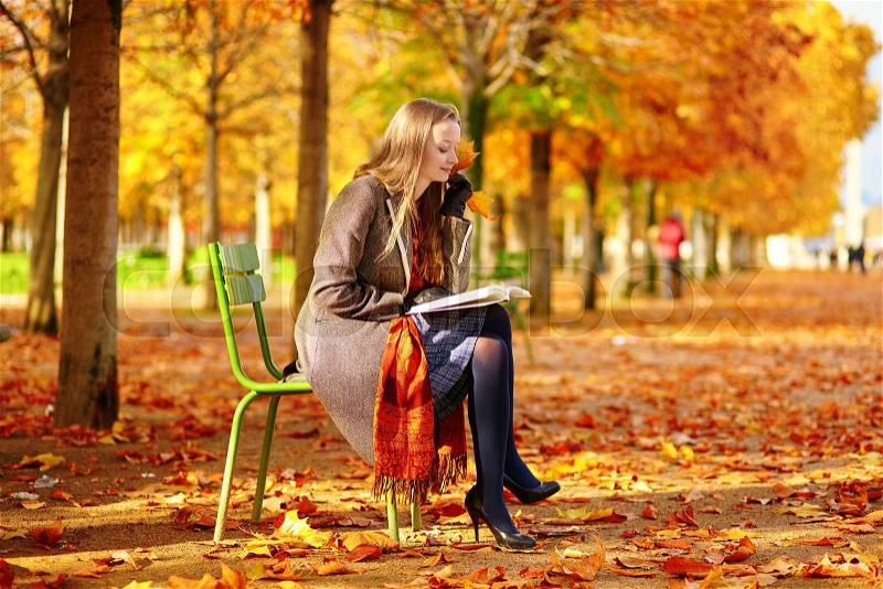 Beautiful young woman in Paris reading in park on a beautiful colorful autumn day, stock photo