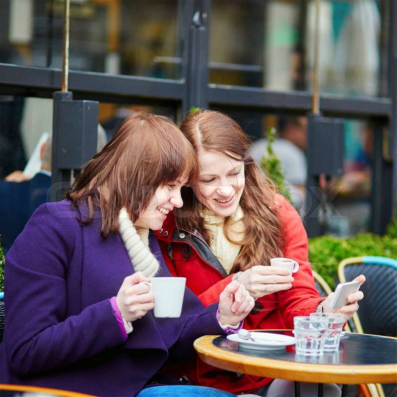 Two cheerful girls making self picture (selfie) in a Parisian street cafe, stock photo