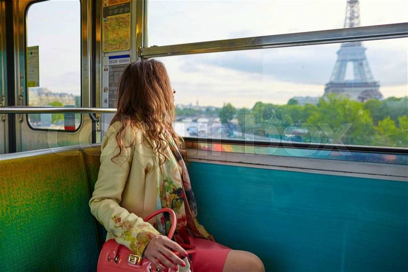 Young beautiful Parisian woman travelling in a subway train, sitting near the window and looking at the Eiffel tower, stock photo