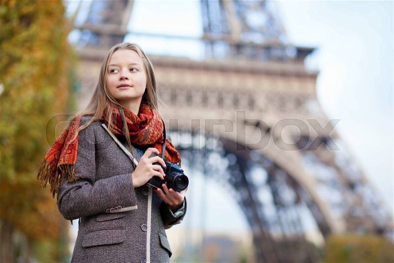 Beautiful girl holding photo camera near the Eiffel tower in Paris, stock photo