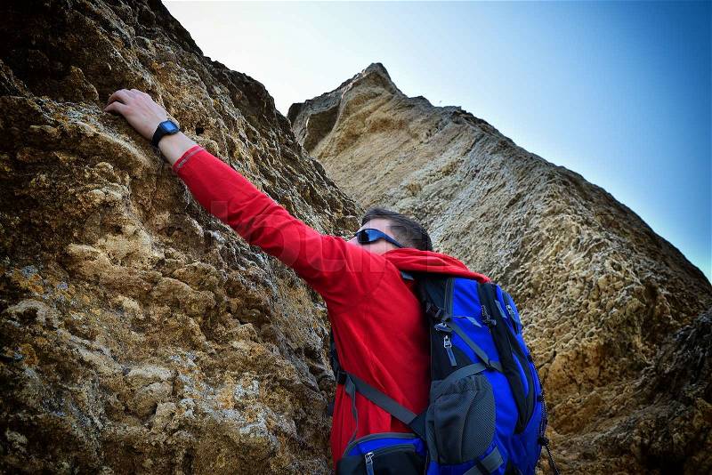 Climber man with backpack hanging on the rock, stock photo