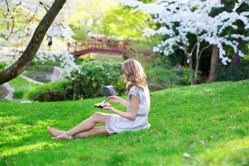 Beautiful young girl eating sushi in cherry blossom garden on a spring day, stock photo