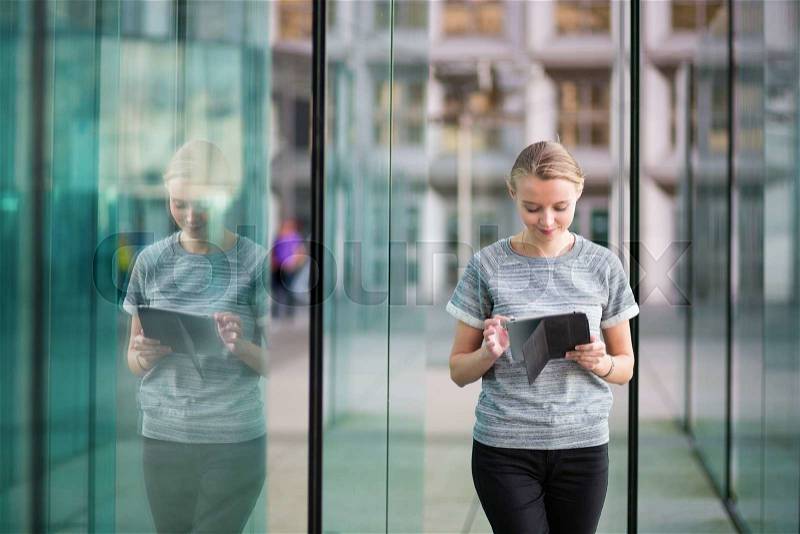 Smiling young woman in modern glass office interior using tablet , stock photo