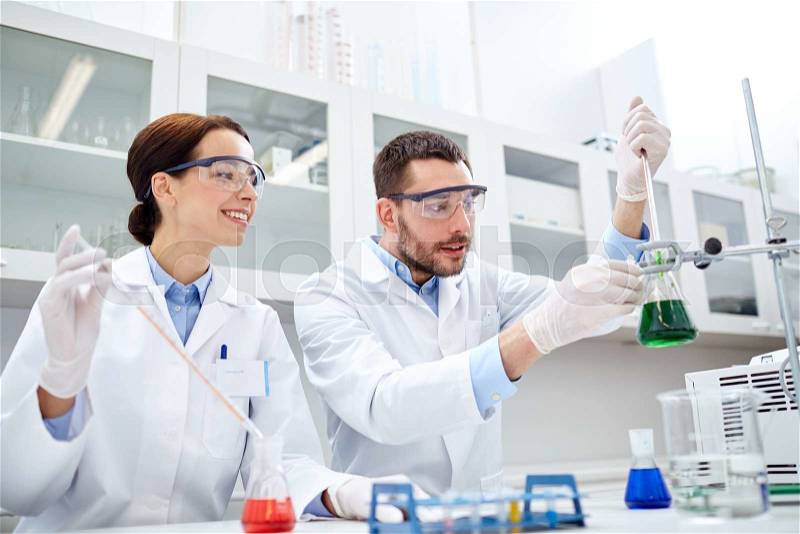 Science, chemistry, biology, pharmacy and people concept - young scientists with pipette and flask making test or research in clinical laboratory, stock photo