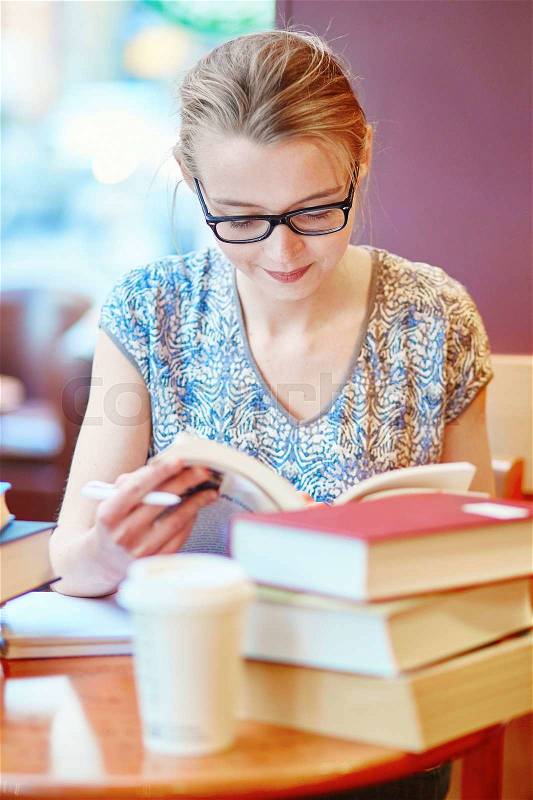 Beautiful young student with lots of books, studying or preparing for exams in a cafe. Shallow DOF, stock photo