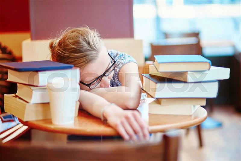 Beautiful young student with lots of books, preparing for exams in a cafe and sleeping on the table tired. Shallow DOF, stock photo