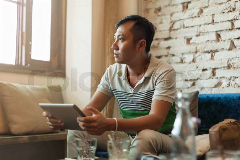 Sad Asian Man Using tablet Computer Sitting at Cafe Depressed Looking to Window, stock photo