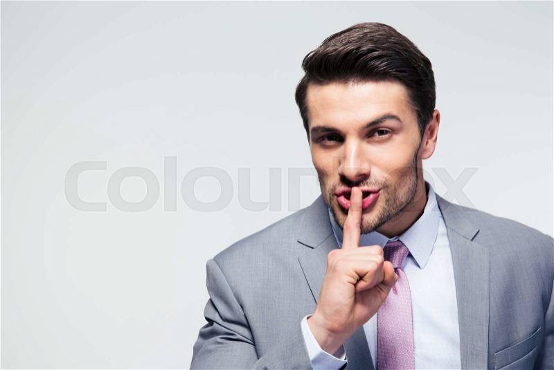 Businessman pointing finger over lips, asking for silence over gray background. Looking at camera, stock photo