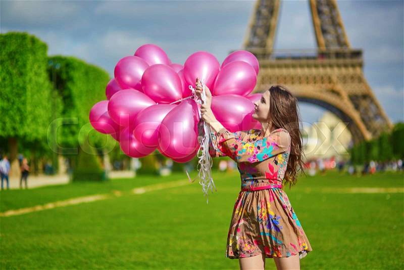 Beautiful young woman near the Eiffel tower in Paris with huge bunch of pink balloons, celebrating her birthday or other event, stock photo