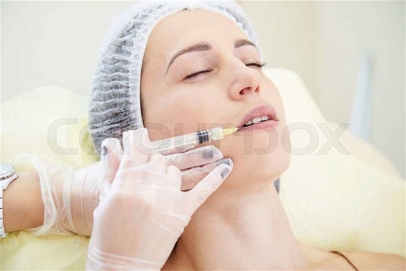 Doctor doing cosmetic injection for young woman, stock photo