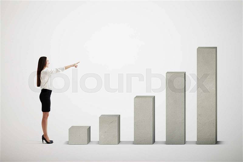 Smiley businesswoman pointing at top of concrete diagram over light grey background, stock photo