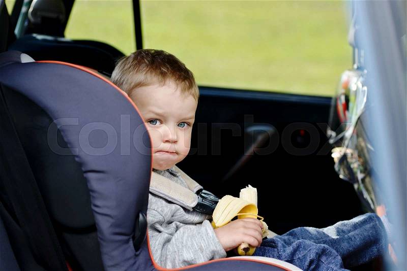 toddler boy sitting in the car seat and eating a banana, stock photo