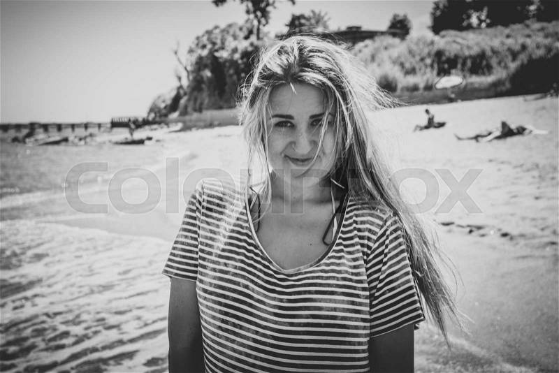 Black and white toned portrait of cute woman with long hair in striped sailor shirt posing on beach, stock photo