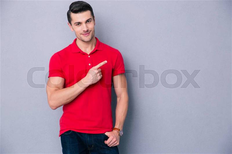 Portrait of a casual man pointing away over gray background, stock photo