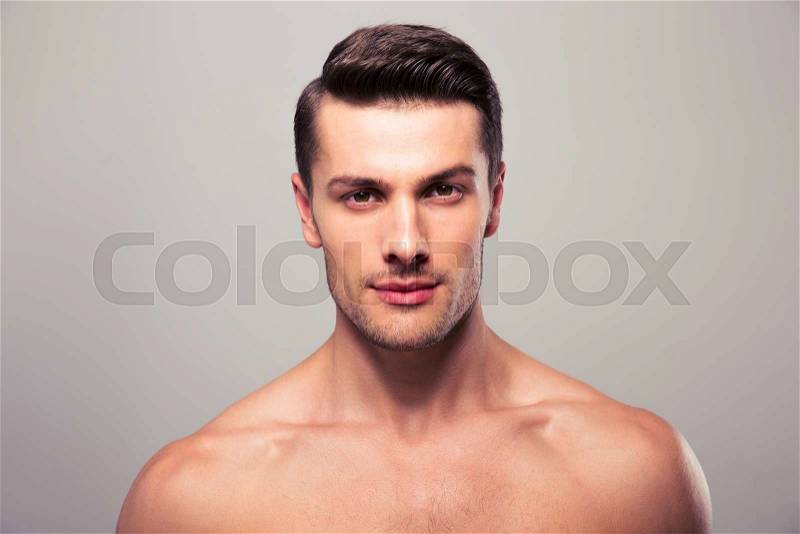 Handsome young man with nude torso looking at camera over gray background, stock photo