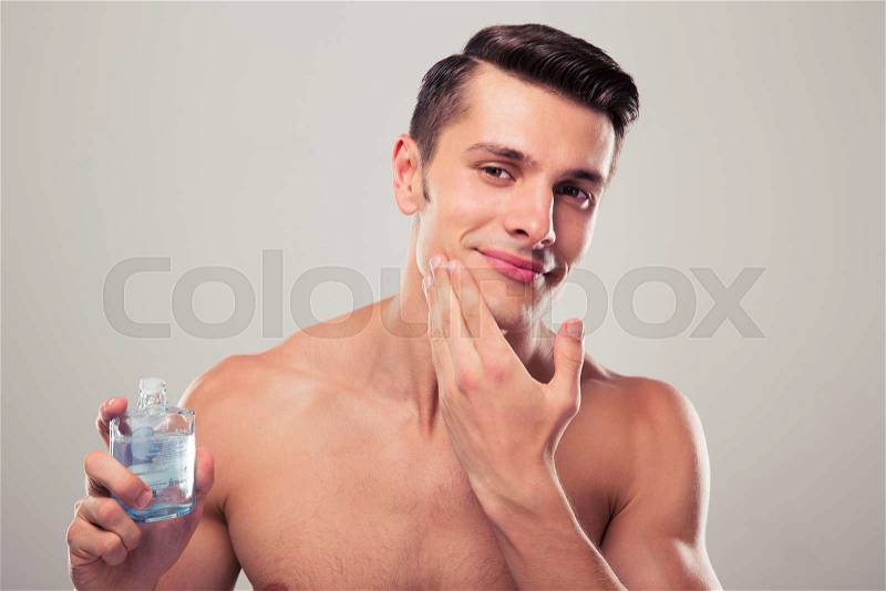 Happy man applying lotion after shave on face over gray background, stock photo