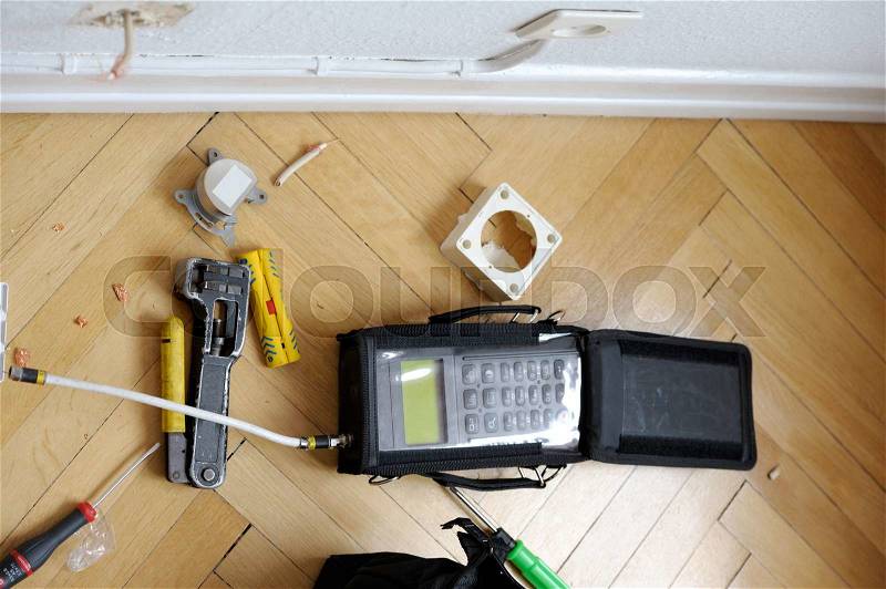 Network and spectrum analyzers and other tools on wooden parquet floor next tot electrical and antenna wall sockets just after installation of digital fiber optic cable for high speed internet, telephone and digital UHD television signal, stock photo