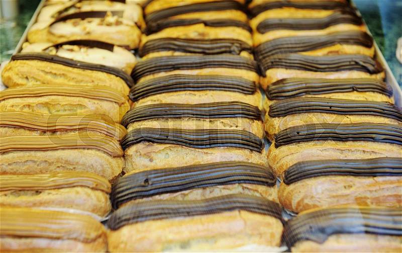 Tasty eclairs on in french bakery store in three rows, with cacao, brown and black chocolate, stock photo