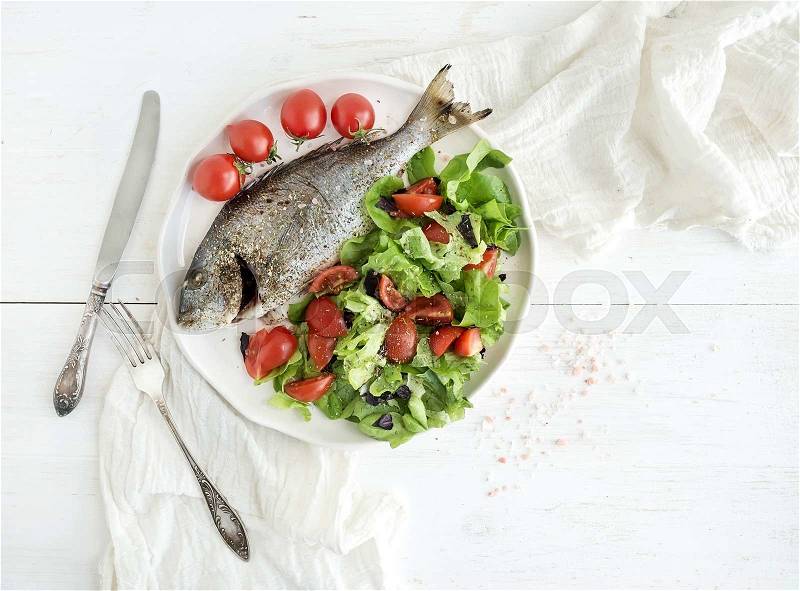 Cooked sea bream fish with fresh vegetable salad on ceramic plate over white rustic wooden backdrop, top view, copy space , stock photo