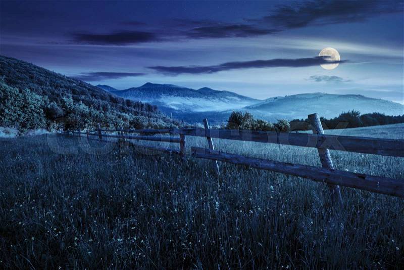 Rural landscape. fence on the hillside meadow shot with ultrawideangle lense. forest in fog on the mountain top at night in full moon light, stock photo