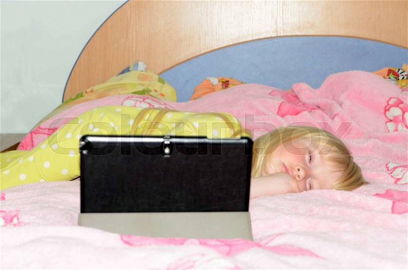 Cute Blond Little Girl Lying on her Stomach While Sleeping on her Bed with Tablet Computer on a Stand, stock photo