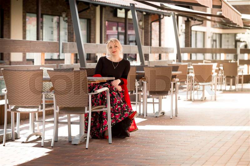 Elegant blonde woman in long dress sitting on summer terrace at cafe, stock photo