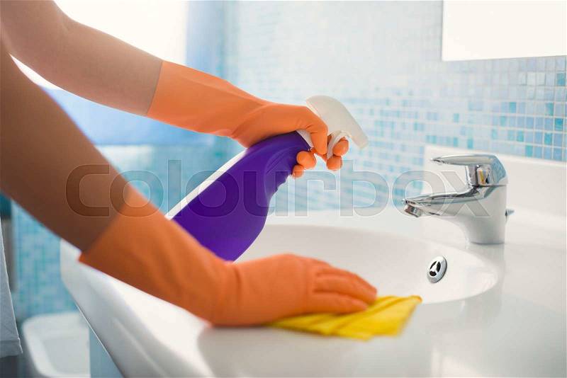 Woman doing chores in bathroom at home, cleaning sink and faucet with spray detergent. Cropped view, stock photo