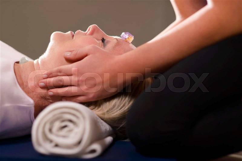 Reiki therapy with girl working as spirit healer, arranging crystals and gemstones on female client for treatment, stock photo