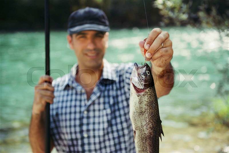 Mid adult fisherman on holidays on river, relaxing and fishing trout. Focus on fish, stock photo