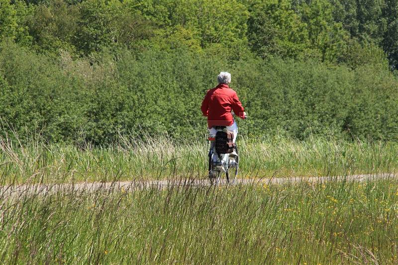 The solitary woman with red coat cycling over the bike path in the park in spring, stock photo