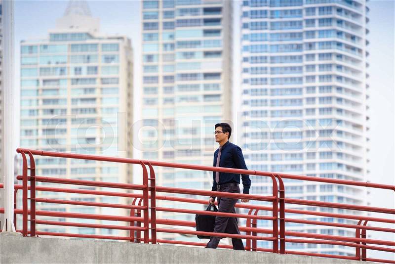 Portrait of chinese businessman walking on bridge in Panama, commuting to work. Skyscrapers in background, stock photo