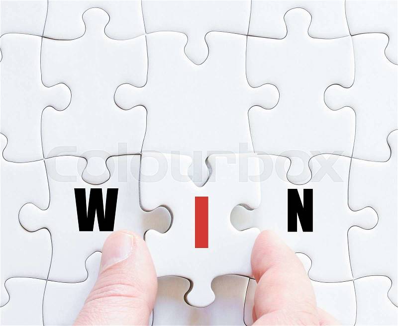 Hand of a business man completing the puzzle with the last missing piece.Concept image of puzzle board with motivational word WIN, stock photo