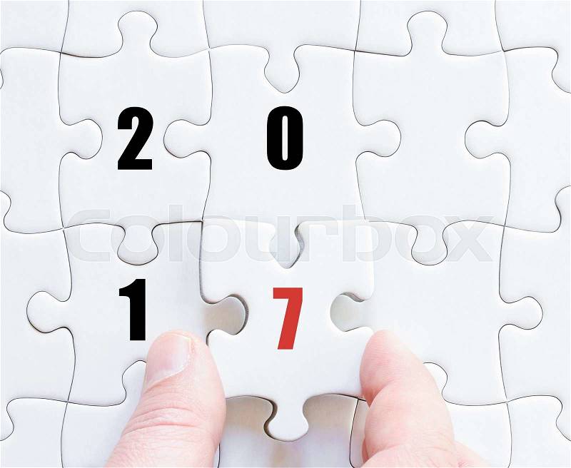 Hand of a business man completing the puzzle with the last missing piece. Concept image of puzzle board with year 2017, stock photo