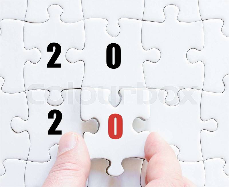 Hand of a business man completing the puzzle with the last missing piece. Concept image of puzzle board with year 2020, stock photo