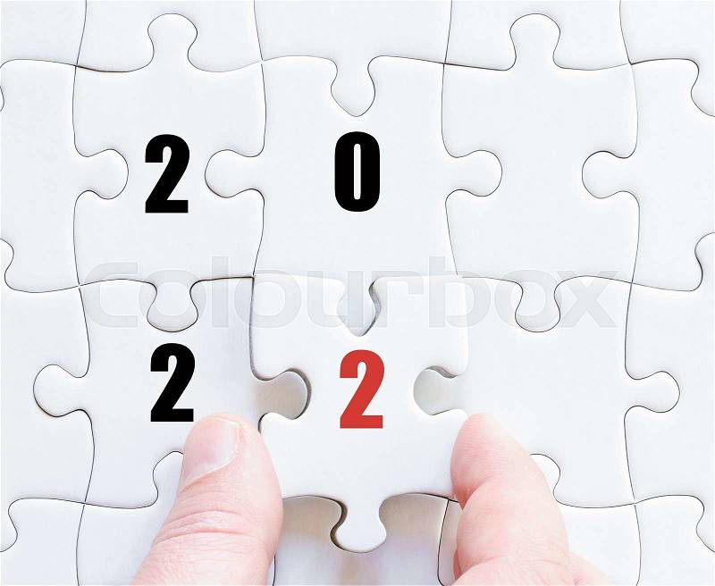 Hand of a business man completing the puzzle with the last missing piece. Concept image of puzzle board with year 2022, stock photo