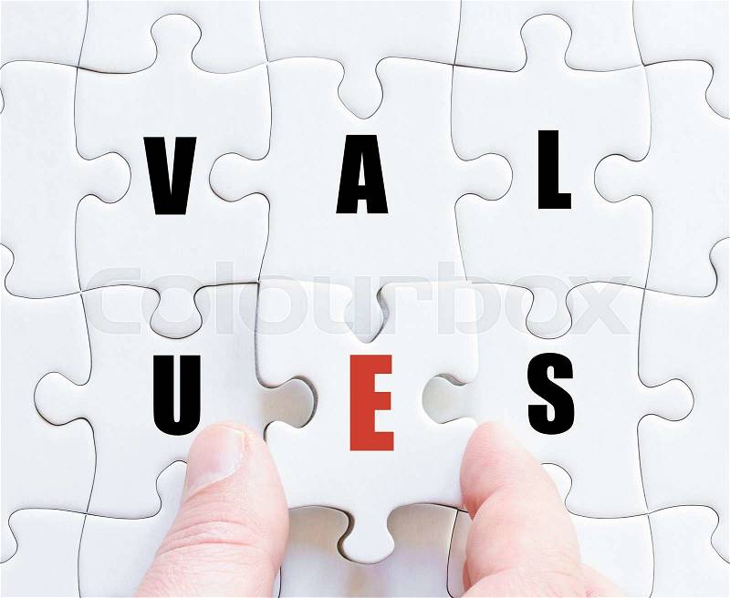 Hand of a business man completing the puzzle with the last missing piece.Concept image of puzzle board with motivational word VALUES, stock photo