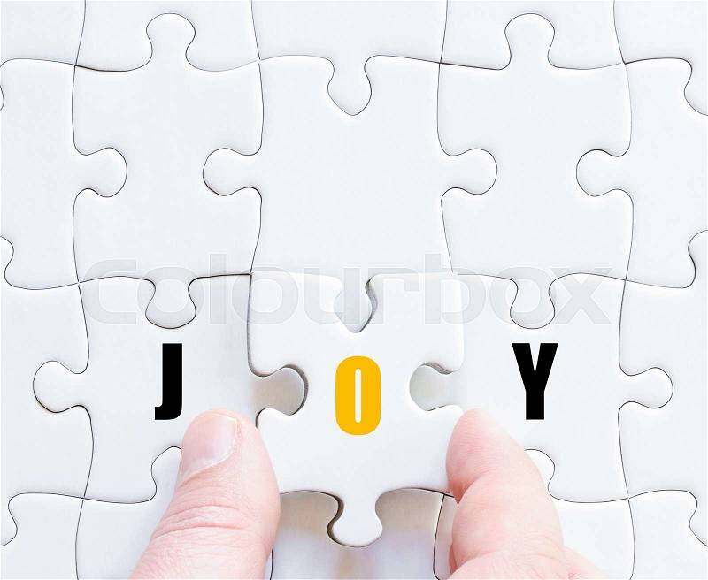 Hand of a business man completing the puzzle with the last missing piece.Concept image of puzzle board with motivational word JOY, stock photo