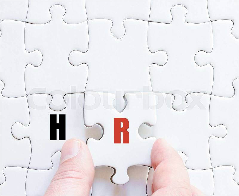 Hand of a business man completing the puzzle with the last missing piece.Concept image of Business Acronym HR as Human Resources, stock photo
