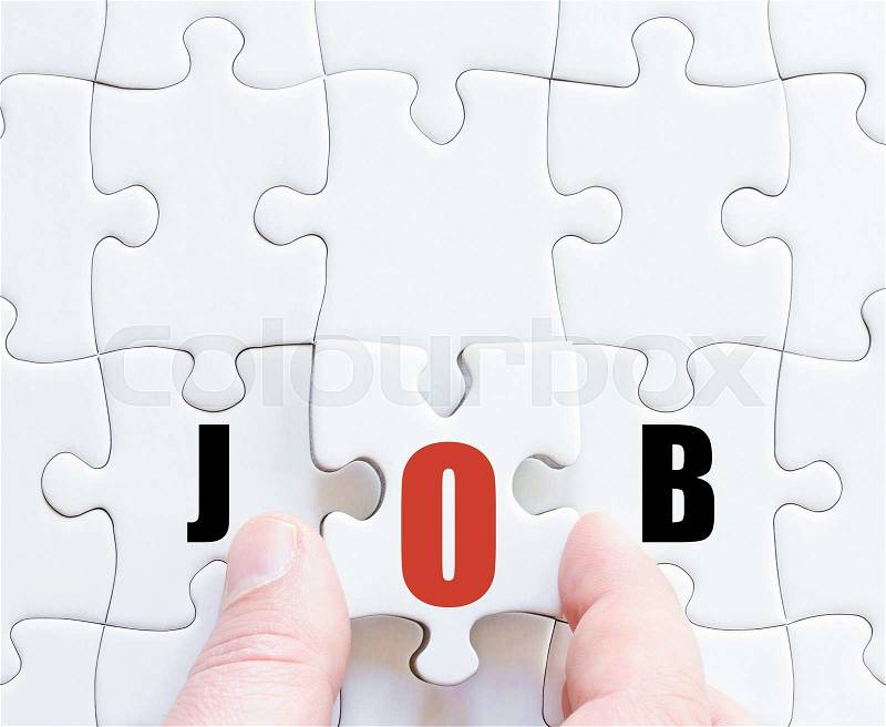 Hand of a business man completing the puzzle with the last missing piece.Concept image of puzzle board with motivational word JOB, stock photo