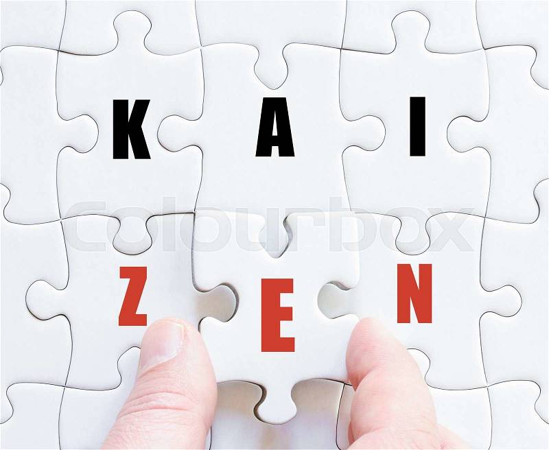 Hand of a business man completing the puzzle with the last missing piece.Concept image of puzzle board with business word KAIZEN, stock photo