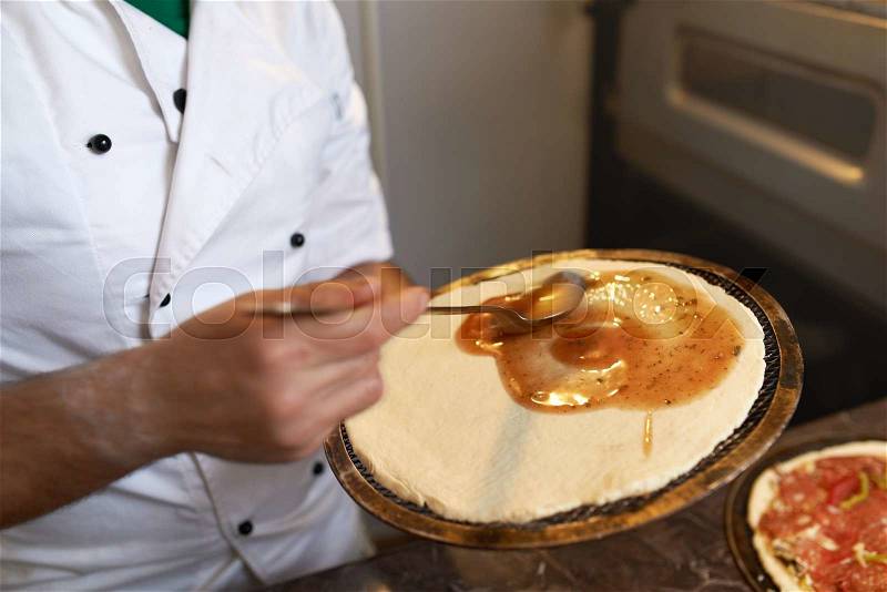 Chef preparing a pizza spreading sauce on the pancake, stock photo