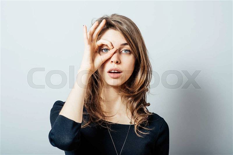 Young happy woman holding her hand over her eye as glasses and looking through fingers, stock photo