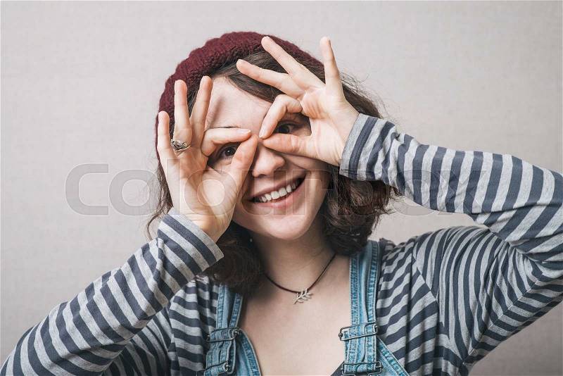Young happy woman holding her hands over her eyes as glasses and looking through fingers, stock photo