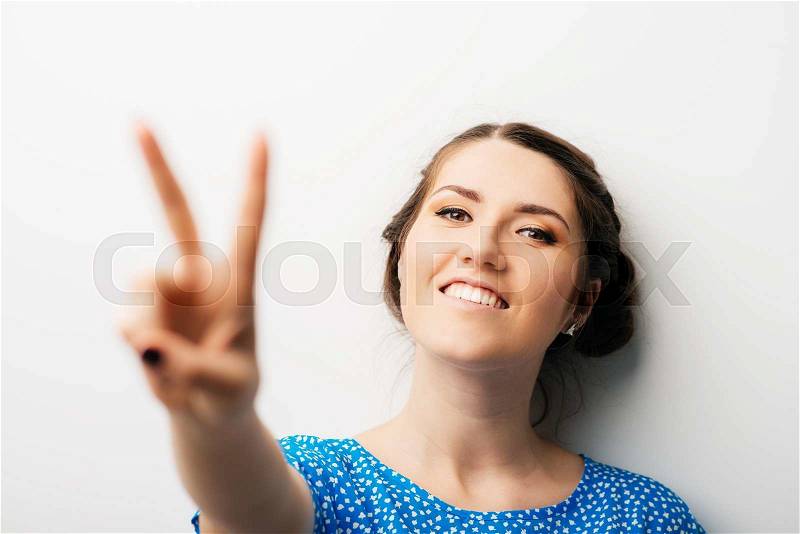 Young woman showing two fingers, positive or peace gesture, on white, stock photo
