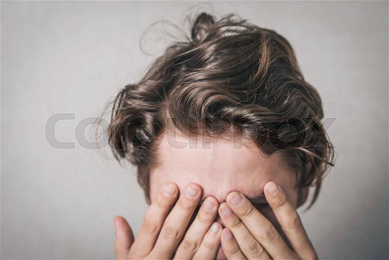 The man was crying, very upset, he covered his face with his hands. Gray background, stock photo