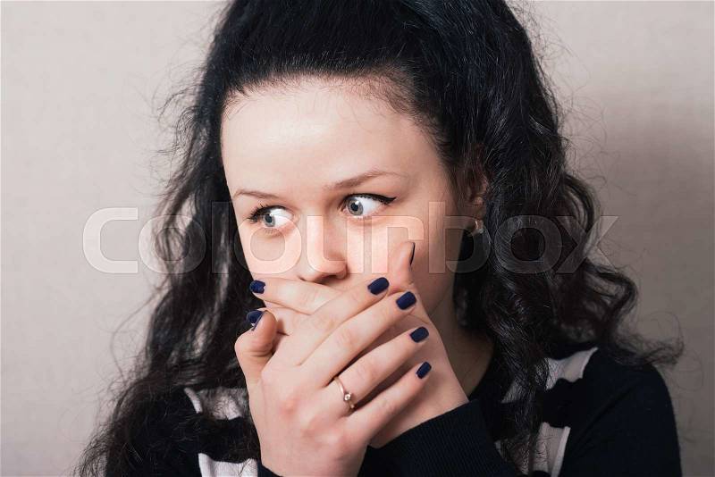 Woman with long hair covering her face with her hands. Gray background, stock photo