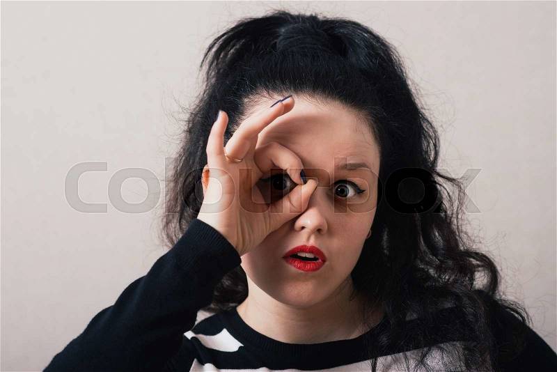 A woman with long hair with hand over eyes, looking through fingers, stock photo