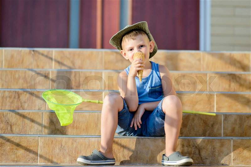 Young Boy with Bug Net Enjoying Ice Cream on Front Steps of Home Sitting in Bright Summer Sunshine, stock photo