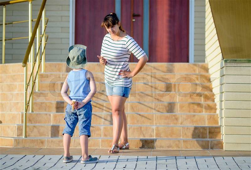 Angry Mother Scolding Son in front of Home - Young Boy Hiding Ice Cream Cone Behind Back and Getting into Trouble, stock photo