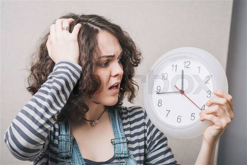 A woman looks at the big clock and holding his head, is late. Gray background, stock photo